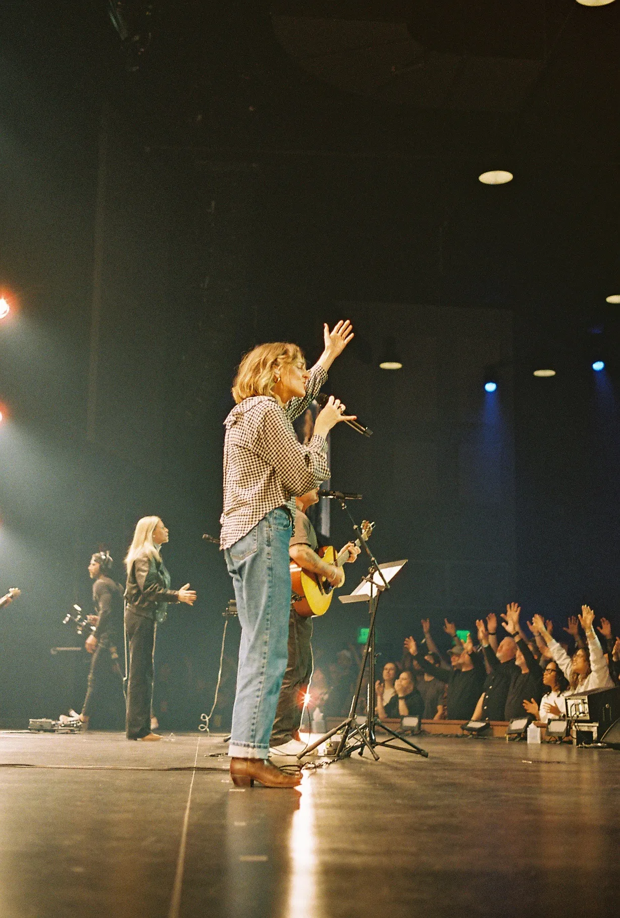 A close-up of hands holding a phone, photographing a crowded concert-style venue.