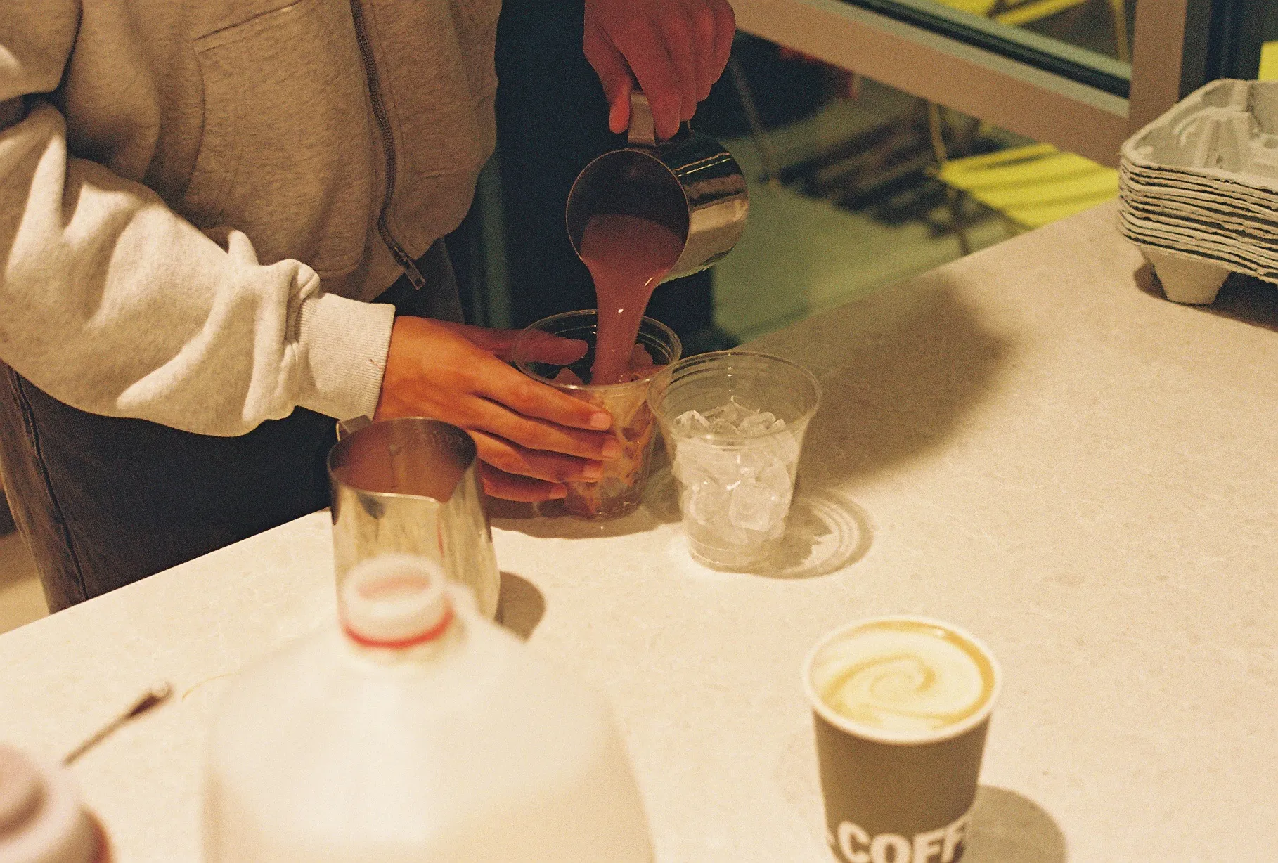 A film photo of hands pouring a drink over ice at a coffee bar.