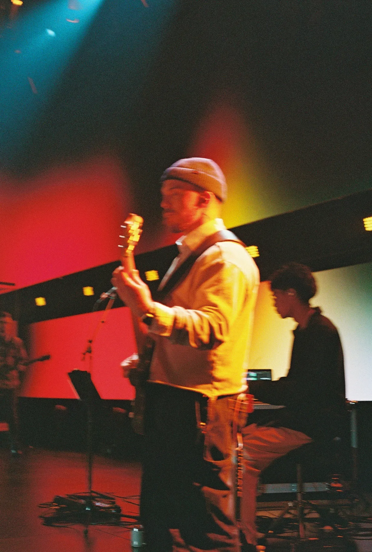 A blurred, warmly lit film photo of a musician playing guitar on stage.